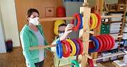 Zwei Frauen interagieren mit einem Holzspielgerät und bunten Ringen.