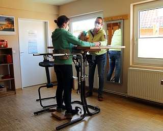 Zwei Personen in einem Raum mit therapeutischem Gerät und Materialien.