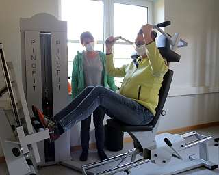 Eine Person nutzt ein Fitnessgerät mit Anleitung einer Trainerin.
