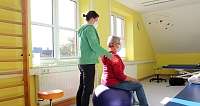 Eine Physiotherapeutin unterstützt einen Patienten auf einem Gymnastikball.