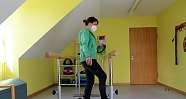 Frau steht auf einem Trainingsgerät in einem Therapieraum.